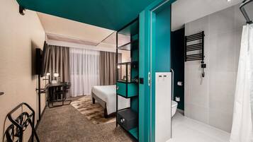 A modern hotel room with a bed, a desk, a TV, a shower, and a bathroom with a towel rack.