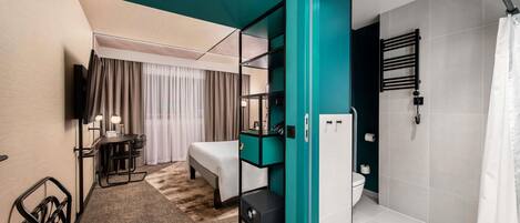 A modern hotel room with a bed, a desk, a TV, a shower, and a bathroom with a towel rack.