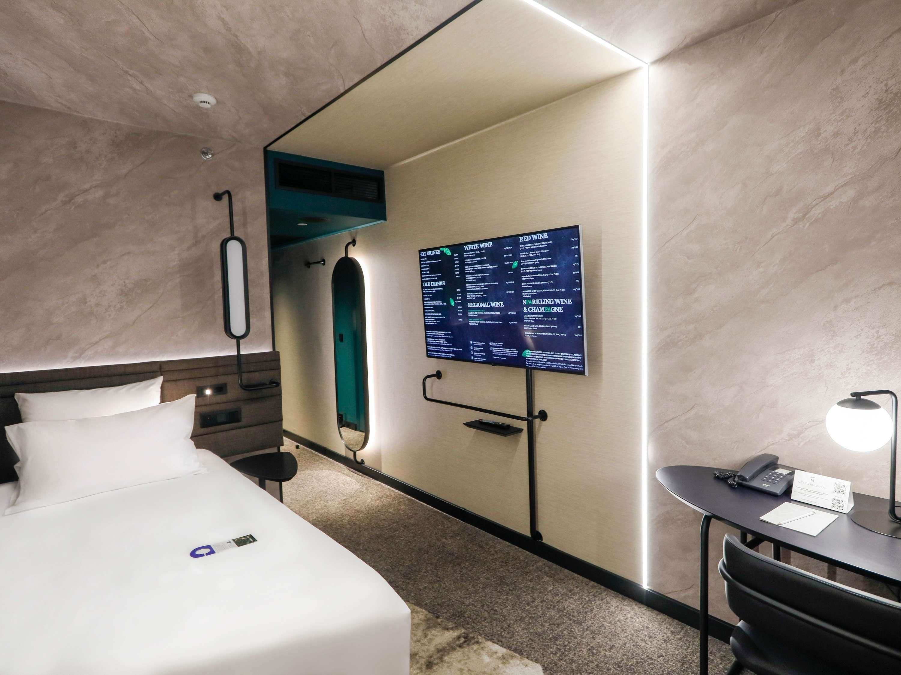 Une chambre d’hôtel équipée d’un lit, d’un bureau, d’une chaise, d’un miroir, d’un téléviseur fixé au mur et d’un téléphone fixé au mur.