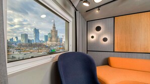 A modern hotel room with a city view, a blue chair, an orange sofa, and a wall with circular light fixtures. - Novotel Warszawa Centrum (Warsaw)