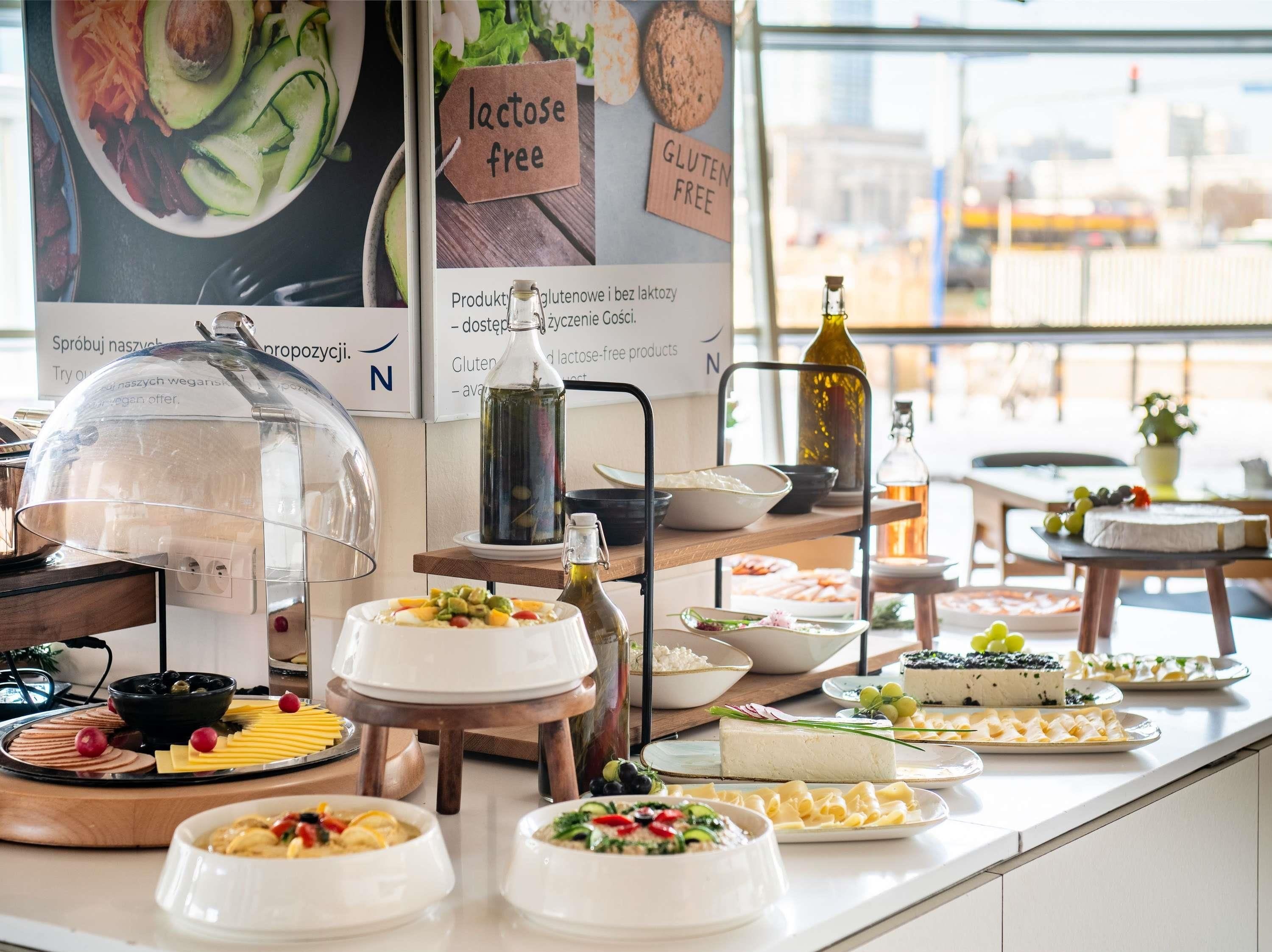 A buffet with various food items, including a cheese board, fruit, and a variety of dishes. There are signs indicating lactose-free and gluten-free options.