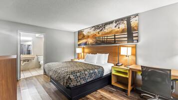 A hotel room with a bed, bedside tables, a desk, a chair, and a large painting on the wall.