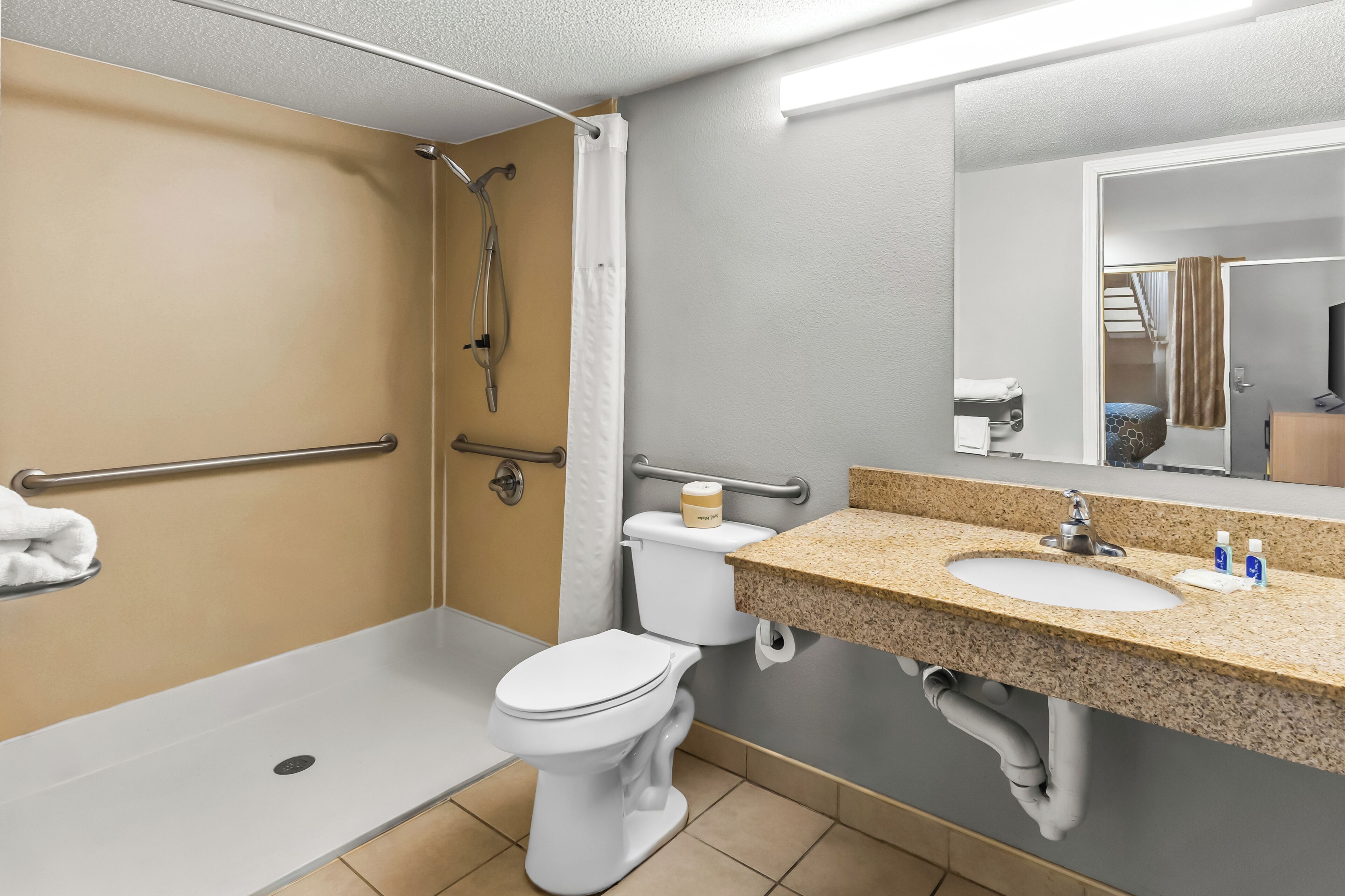 A bathroom with a shower, toilet, sink, and handrails.