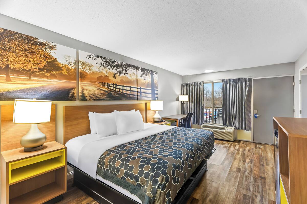 A hotel room with a bed, bedside tables, a desk, a chair, a window with curtains, and a door.