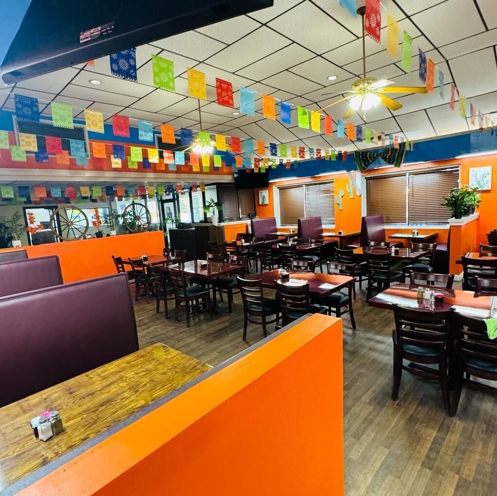 A restaurant with booths and tables, colorful flags, and a ceiling fan.