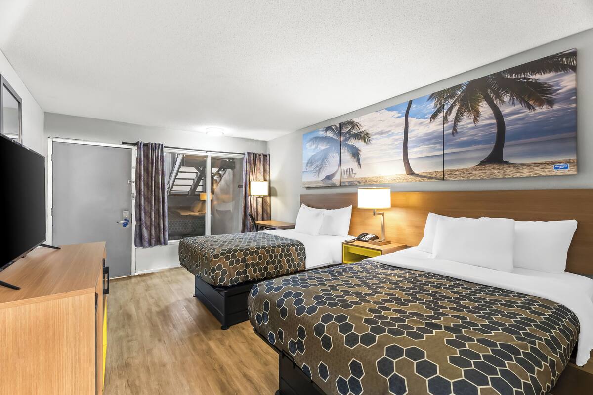 A hotel room with two beds, a TV, a desk, and a painting of a beach scene.
