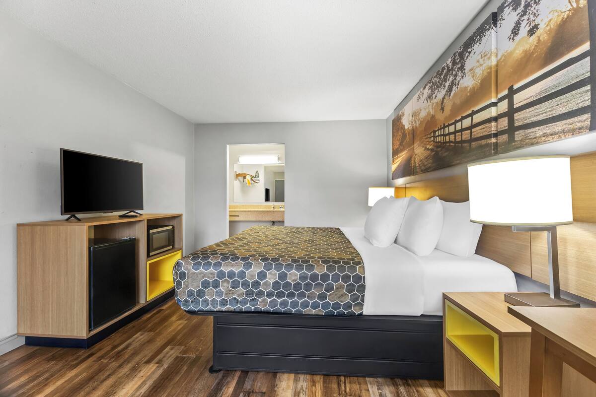 A hotel room with a bed, a TV, a desk, and a mirror.