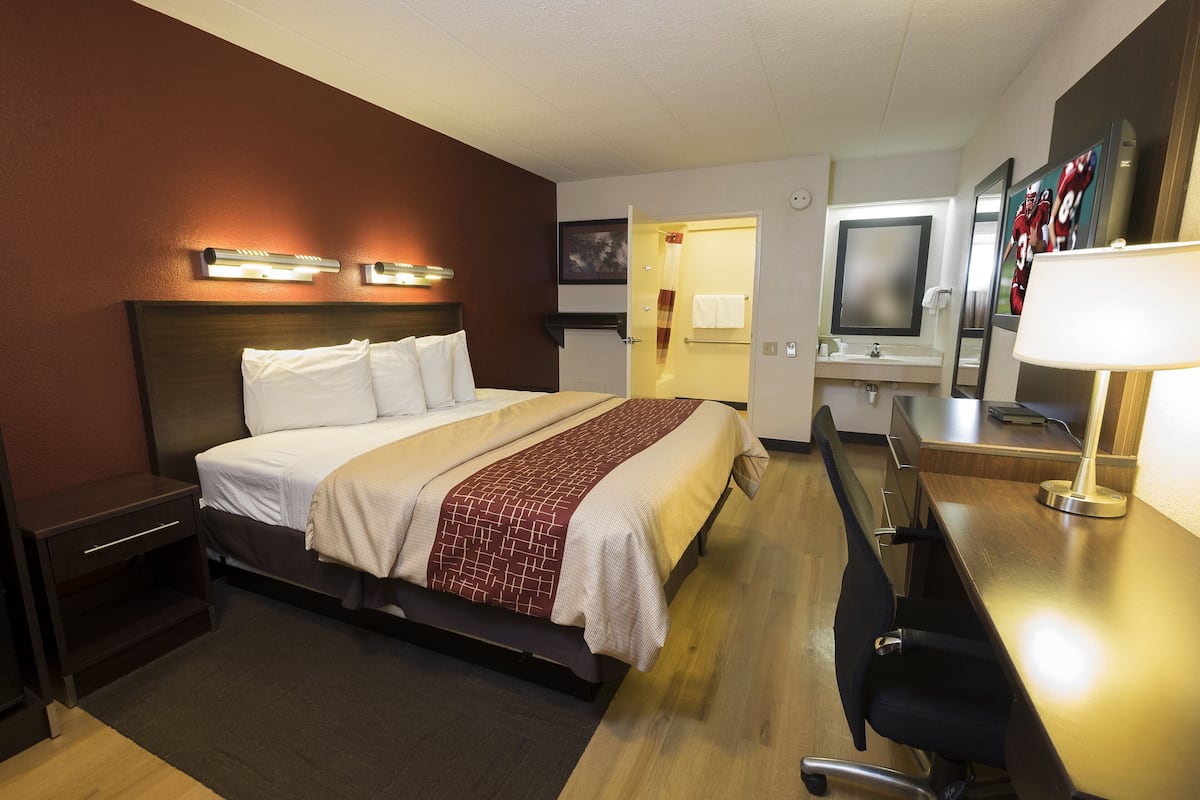 A hotel room with a bed, bedside table, desk, chair, and a mirror.