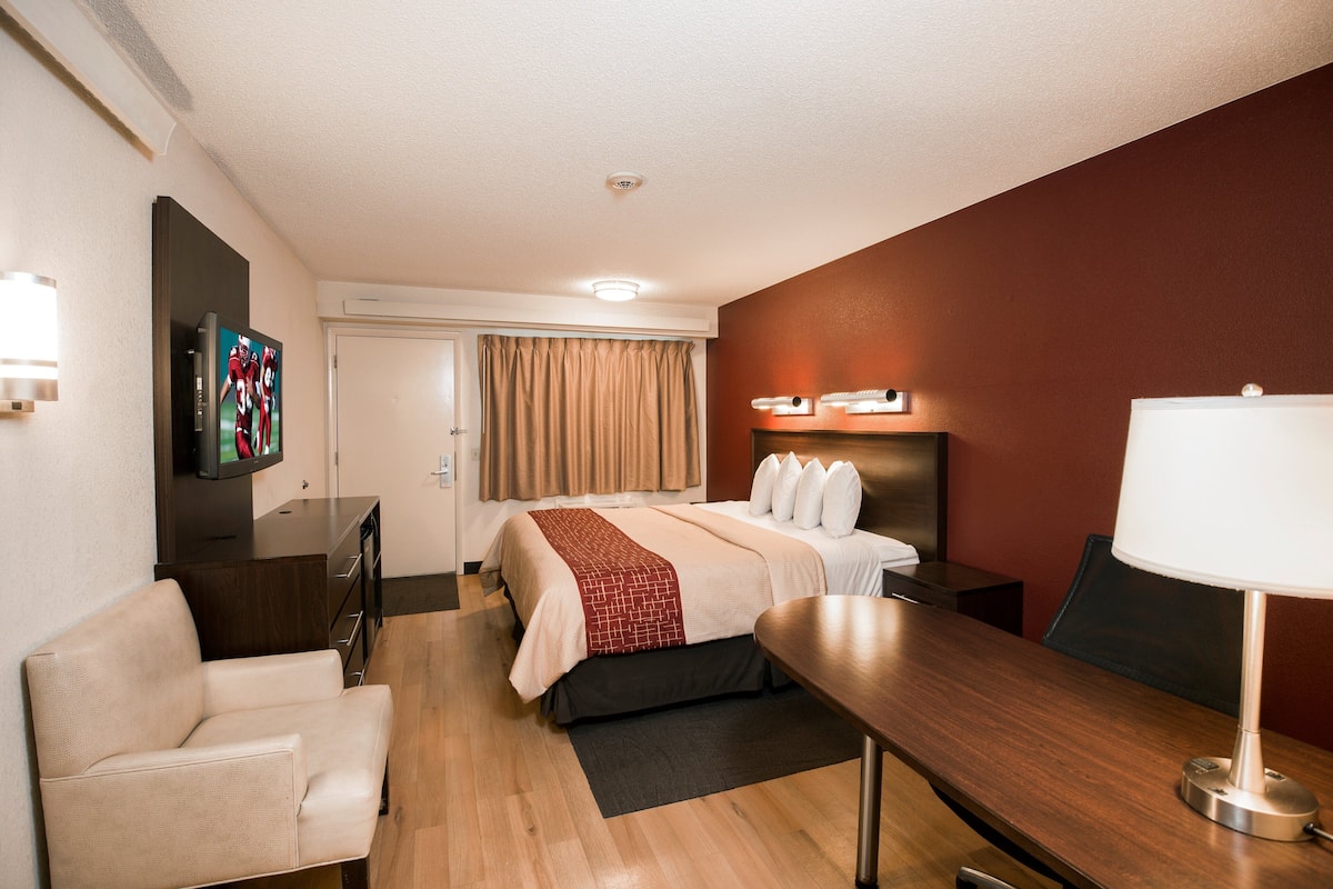 A hotel room with a bed, a desk, a chair, a TV, and a lamp.