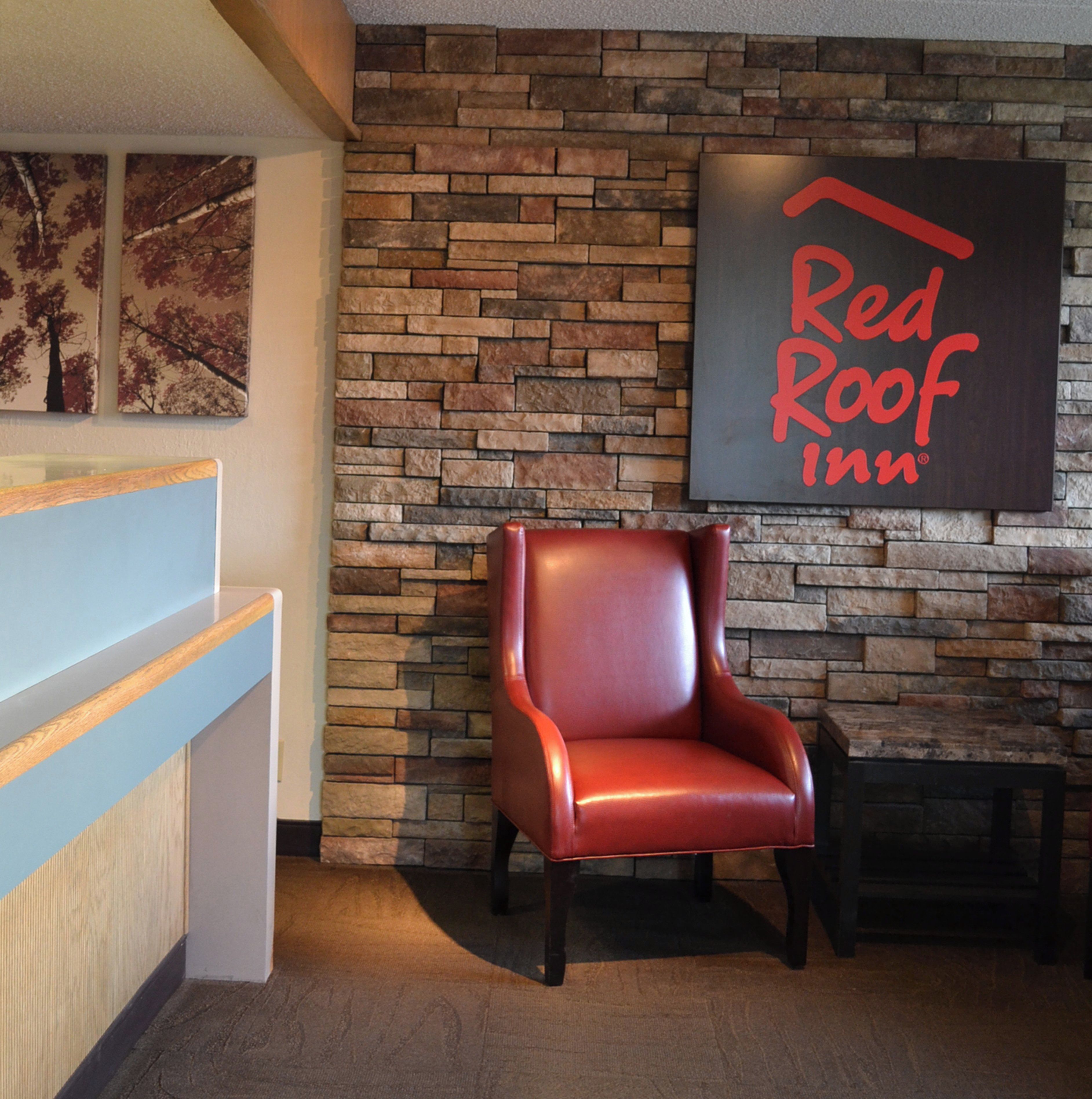 A reception area with a stone wall, a Red Roof Inn sign, a leather chair, and a wooden reception desk.
