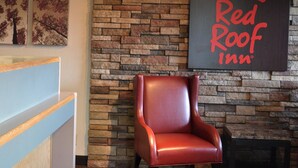 Un área de recepción con pared de piedra, el logotipo de Red Roof Inn, un sillón de cuero y un mostrador de recepción de madera.