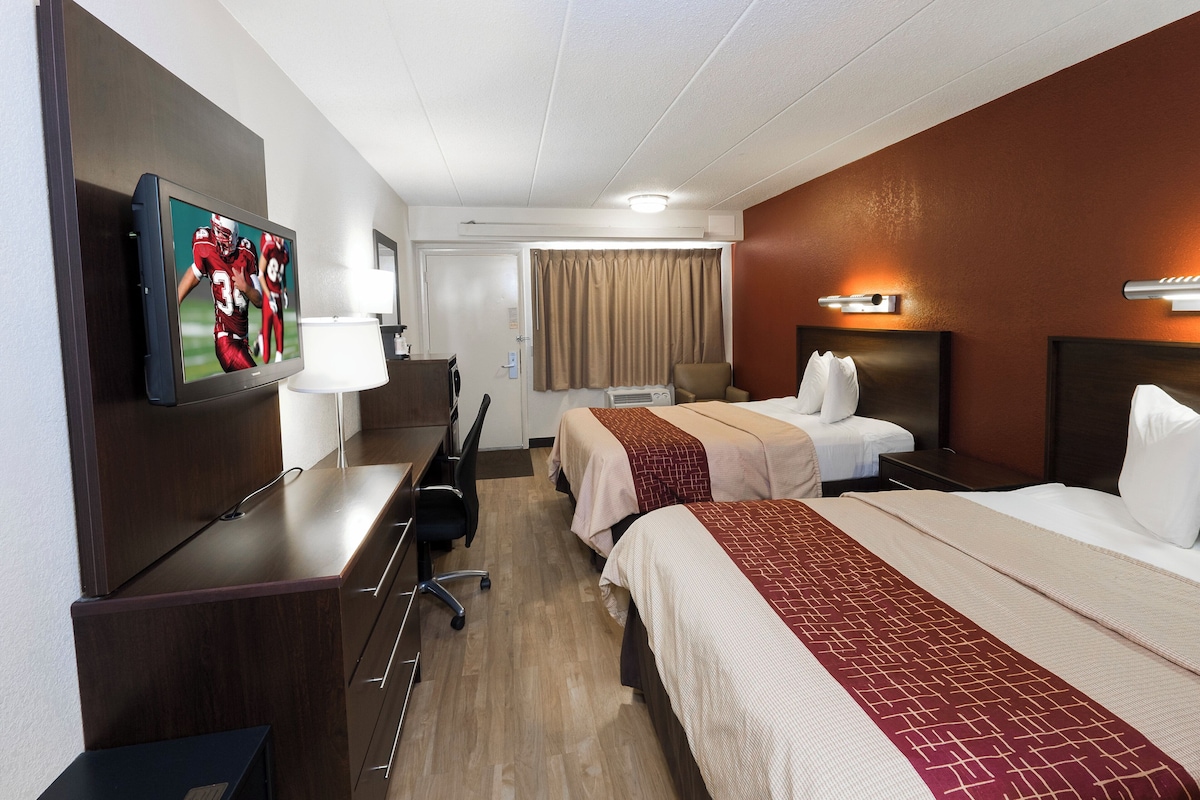 Une chambre d’hôtel équipée d’une télévision, d’un bureau, de deux lits, d’une chaise et d’une fenêtre avec des rideaux.