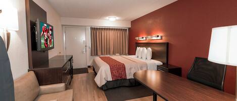 Una habitación de hotel con una cama, un escritorio, una silla, un televisor y una ventana con cortinas.