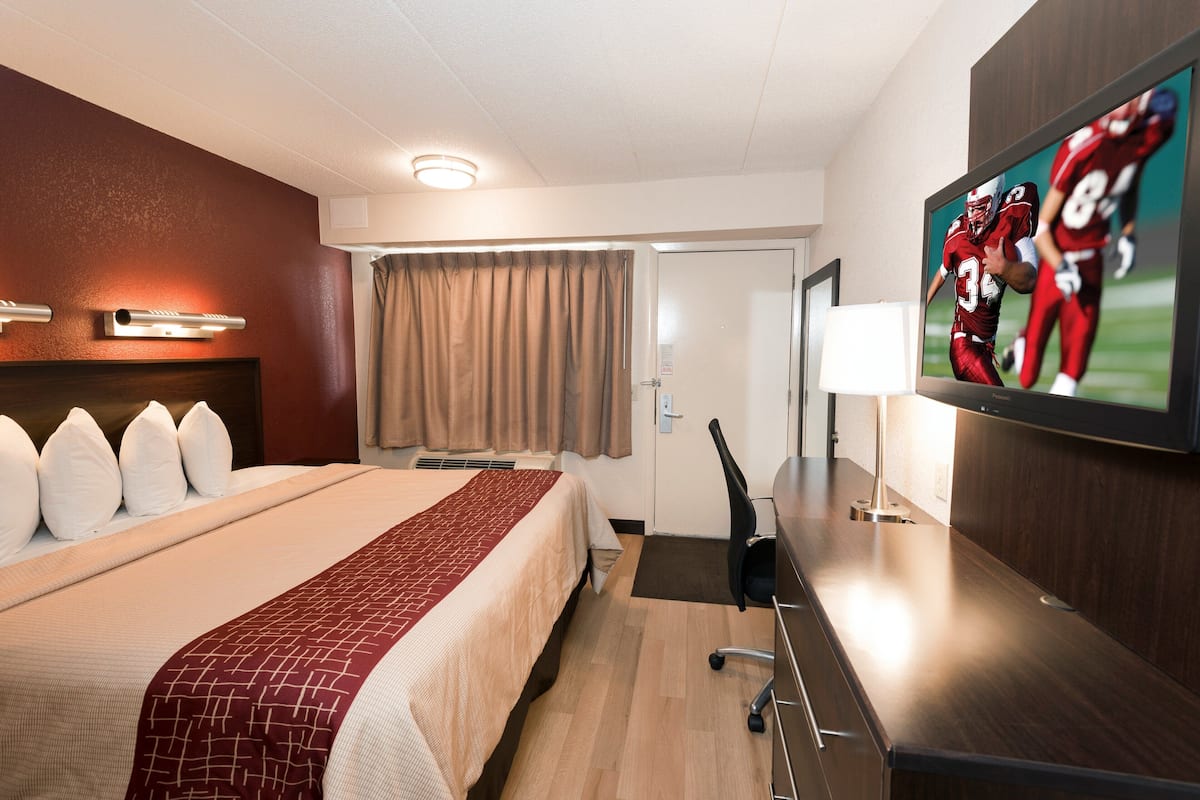 A hotel room with a large bed, a flat-screen TV, a desk with a lamp, and a door.