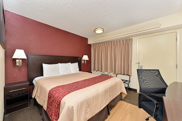 A hotel room with a bed, bedside lamps, a desk, a chair, and a door.