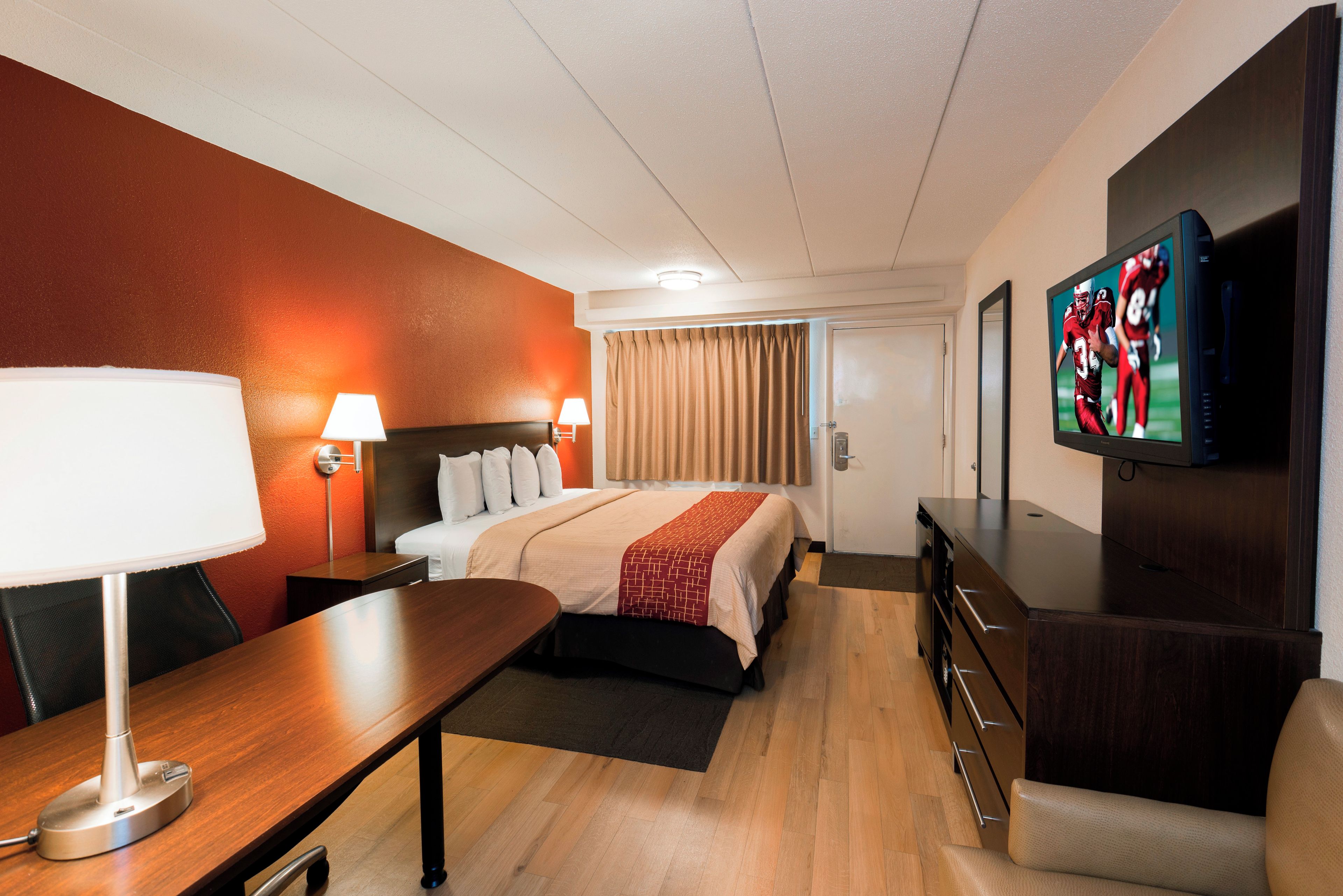 A hotel room with a bed, bedside lamps, a desk, a TV, and a dresser.