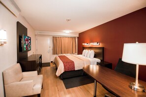 Een hotelkamer met een bed, een bureau, een stoel, een televisie en een wandlamp.