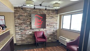 A reception area with a stone wall, a red chair, a reception desk with a digital kiosk, and a window with a view.