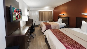 Une chambre d’hôtel équipée d’une télévision, d’un bureau, de deux lits, d’une chaise, d’une lampe et d’une fenêtre avec des rideaux.