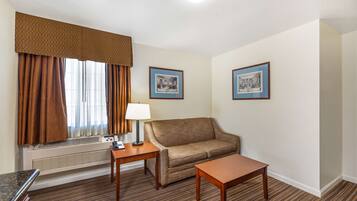 A hotel room with a brown sofa, a small table, a lamp, and two framed pictures on the wall.
