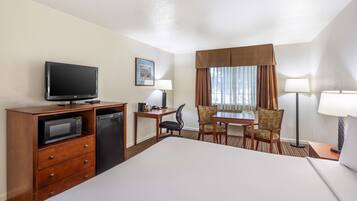 A hotel room with a large bed, a desk with a chair, a television, a microwave, and a refrigerator.