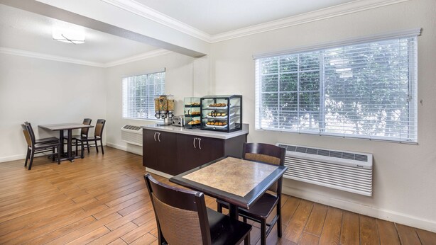 A dining area with a table and chairs, a kitchen counter with appliances, and large windows with blinds. - Best Western Capital City Inn (Sacramento)