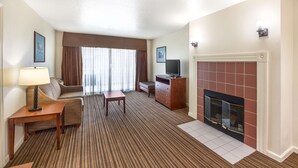 A hotel room with a sofa, a small table, a TV, a fireplace, and a carpeted floor. - Best Western Capital City Inn (Sacramento)