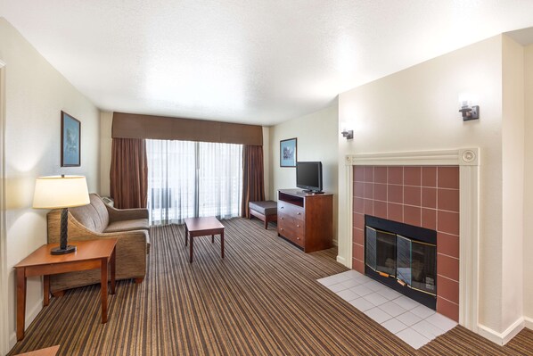 A hotel room with a sofa, a small table, a TV, a fireplace, and a carpeted floor.