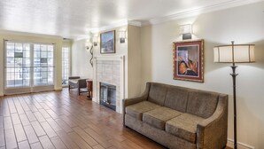 A spacious living room with hardwood flooring, a fireplace, a sofa, and a large window with a view of the street. - Best Western Capital City Inn (Sacramento)