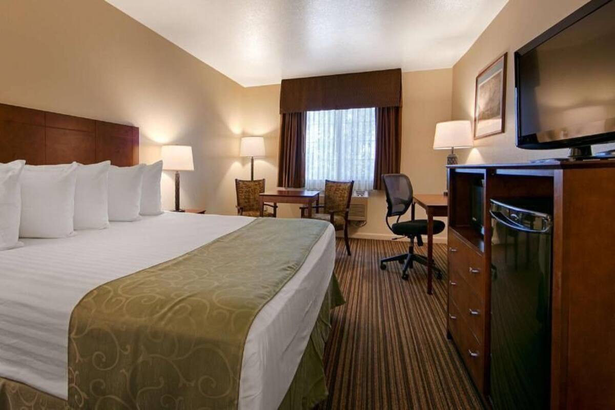 A hotel room with a large bed, a desk, two chairs, a television, and a dresser.