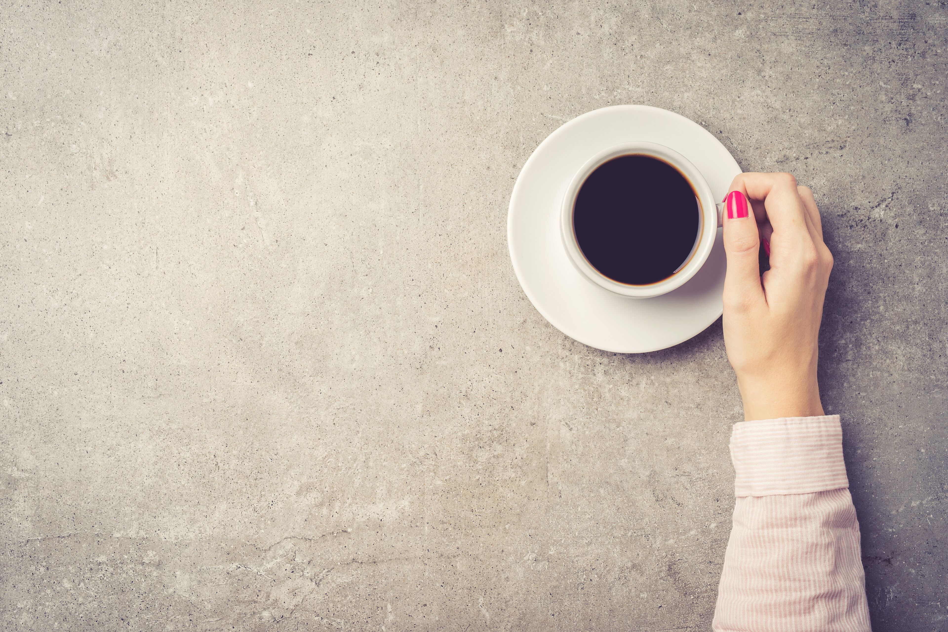 A cup of coffee on a saucer on a textured surface.