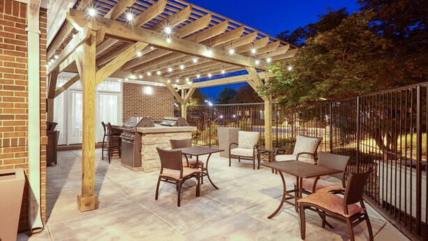 Een terras buiten met een pergola, zitplaatsen en een barbecuehoek.