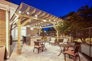 An outdoor patio with a pergola, seating, and a barbecue area.