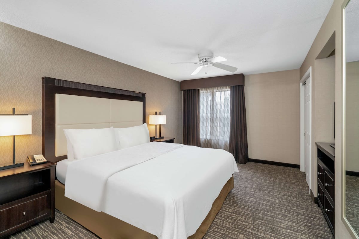 Une chambre d’hôtel avec un grand lit, deux tables de chevet avec des lampes, un ventilateur de plafond et un grand miroir.