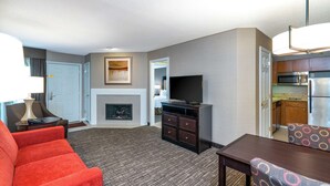 Hotelkamer met een zithoek, bestaande uit een rode bank, een flatscreen televisie, een open haard en een eettafel met gestreept beklede stoelen.