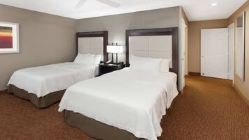 A hotel room with two beds, a ceiling fan, a nightstand with a lamp, and a painting on the wall.