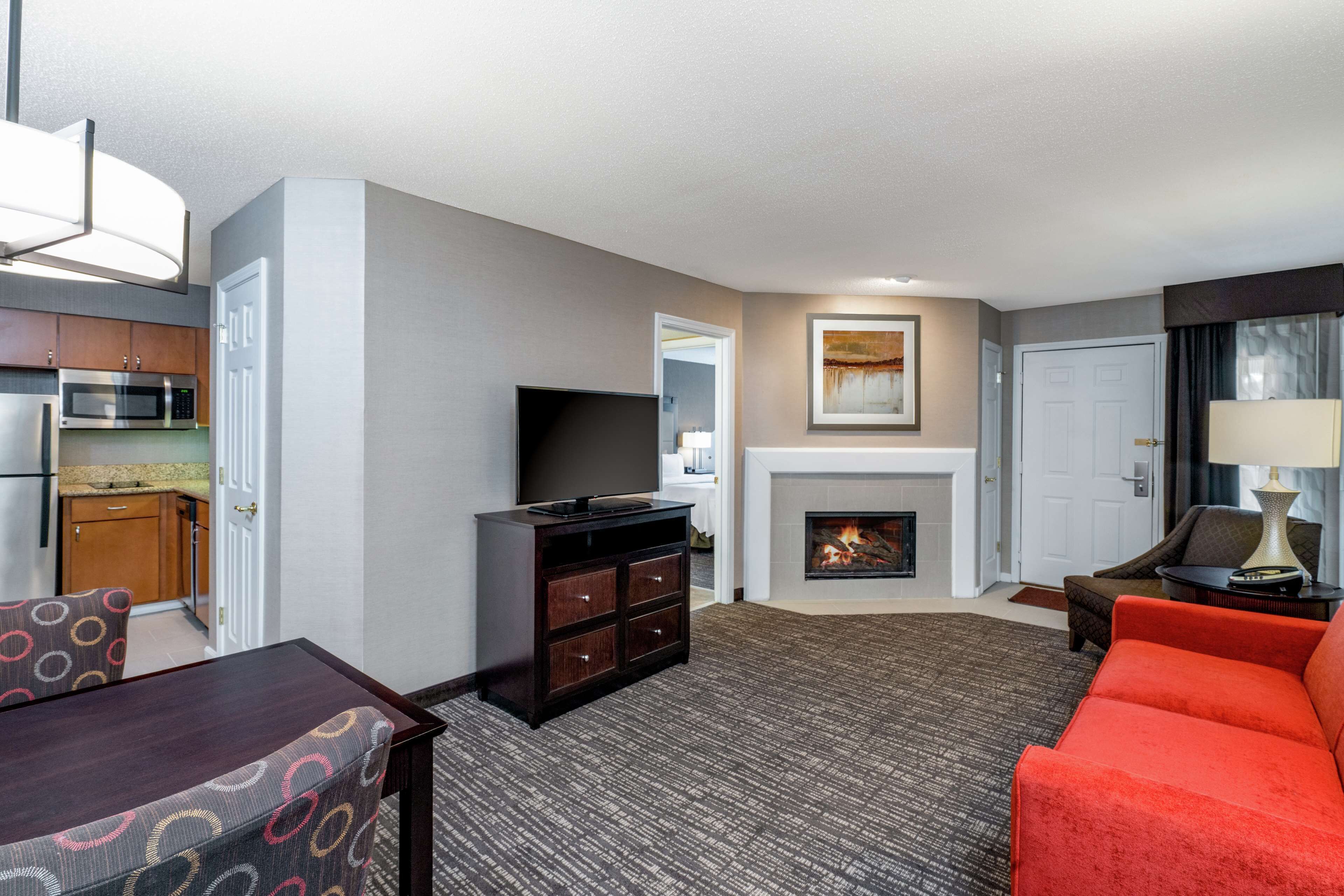 A hotel room with a kitchen area, a fireplace, a television, a dining table, and a sofa.