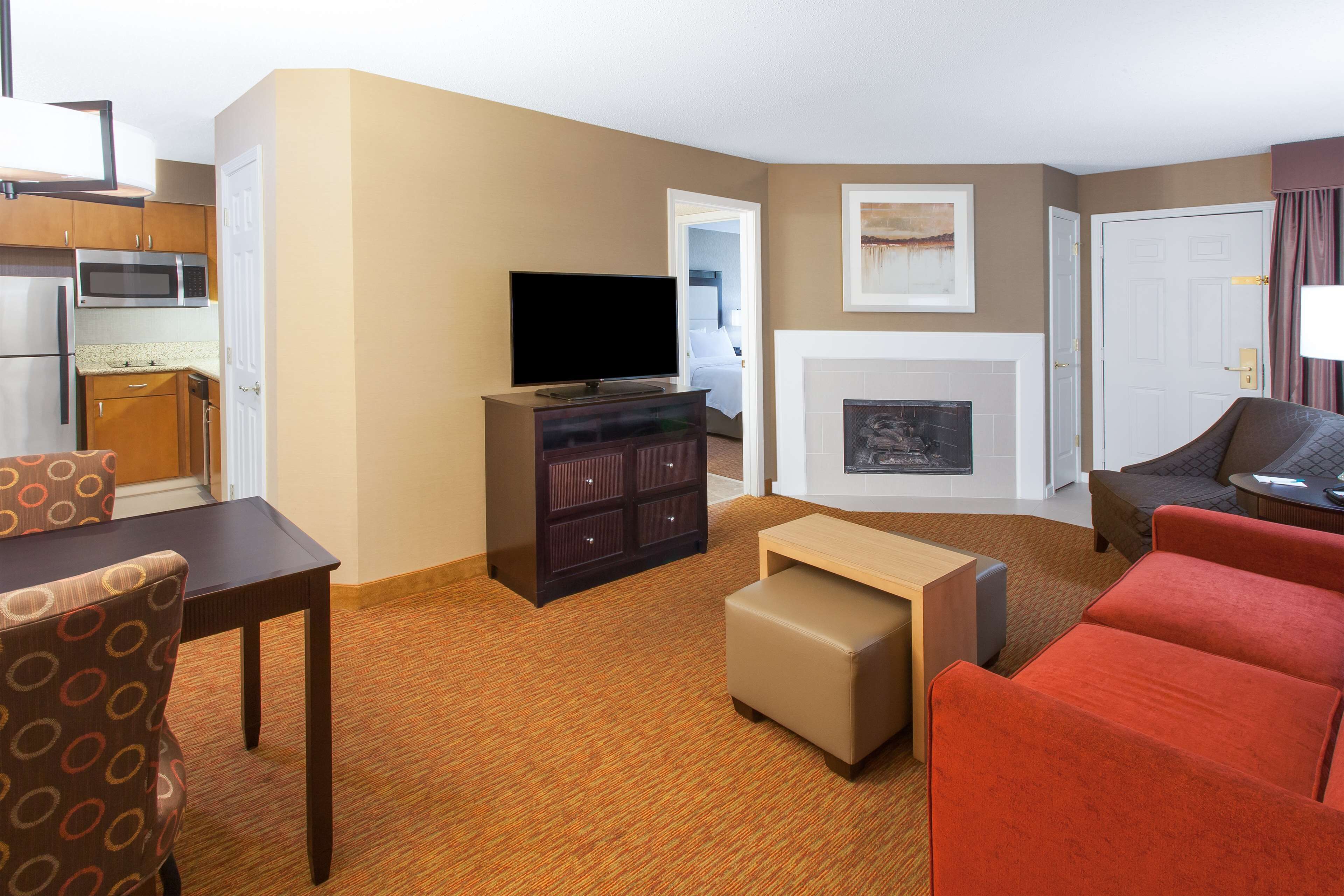 A hotel room with a kitchenette, a flat-screen TV, a fireplace, a sofa, and a dining area with a table and chairs.