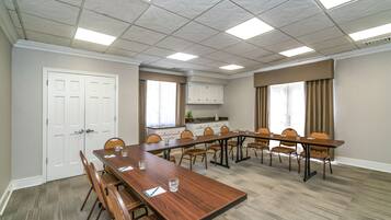 Uma sala de conferências com uma mesa comprida, cadeiras e uma pequena cozinha.