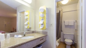 A bathroom with a sink, mirror, towel rack, toilet, and shower. - Cathedral Hill Hotel (San Francisco)