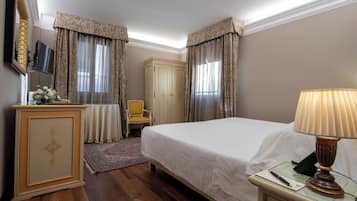 Habitación de hotel con cama, escritorio con lámpara, silla, armario y televisor en la pared.