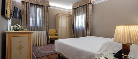 Habitación de hotel con cama, escritorio con lámpara, silla, armario y televisor en la pared.