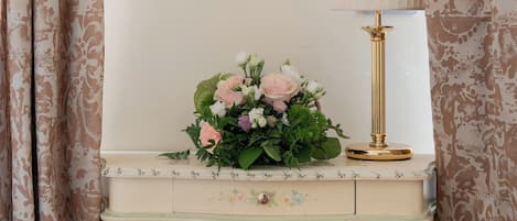 Una habitación con tocador, espejo, lámpara y un arreglo floral.