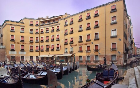 A row of gondolas docked at a canal with a hotel named "Hotel Cavaletto" in the background.