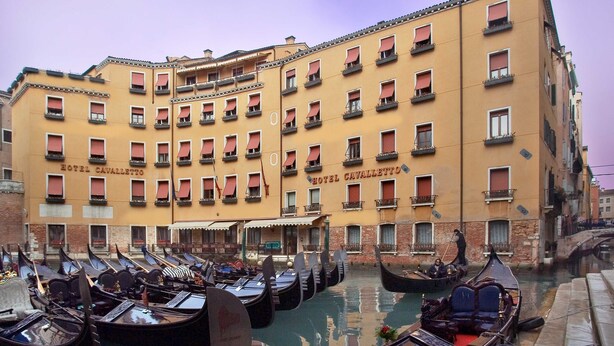Een rij gondels afgemeerd aan een gracht, met hotel 'Hotel Cavaletto' op de achtergrond.