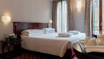 A hotel room with a neatly made bed, a bedside table with a lamp, and a view of the outside through large windows.