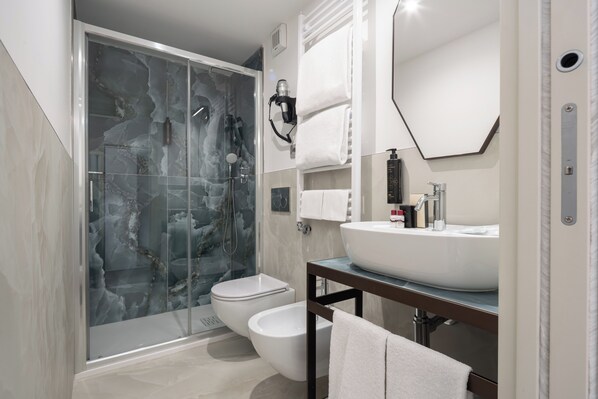 A modern bathroom with a glass-enclosed shower, a white toilet, a bidet, a large mirror, and a vanity with a sink.