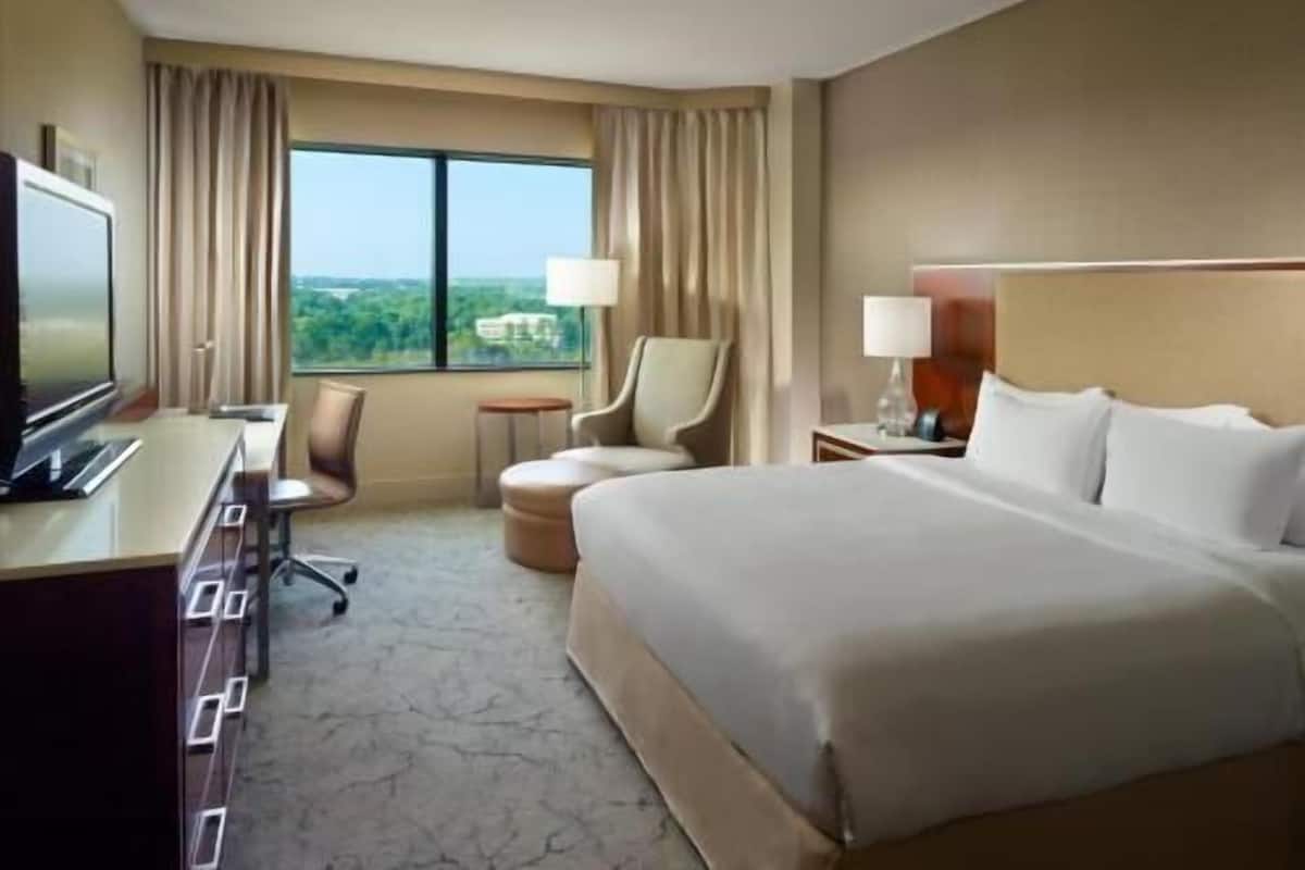 A hotel room with a bed, a desk, a chair, a TV, and a window with curtains.