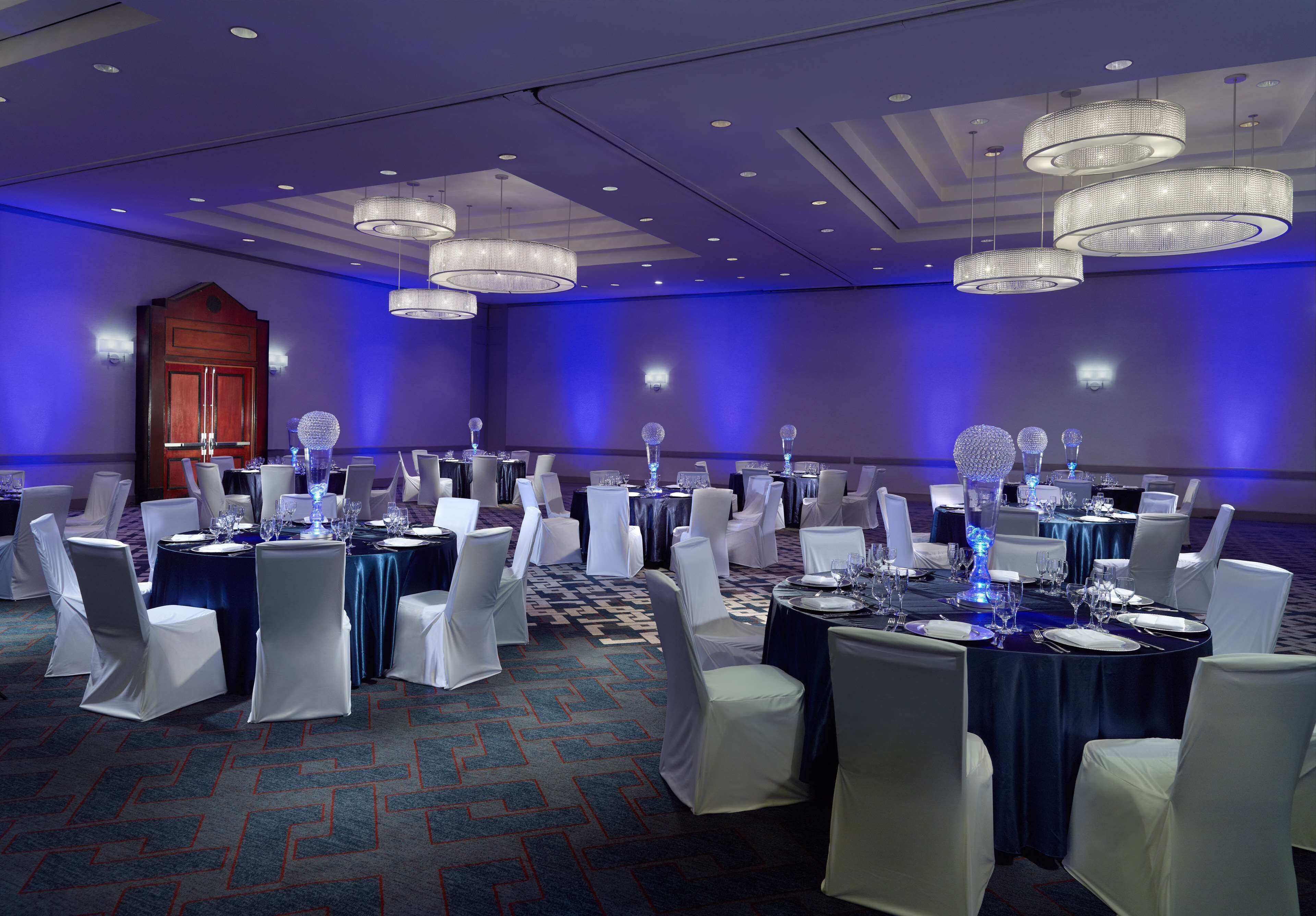 A banquet hall with round tables, white chairs, and blue tablecloths.