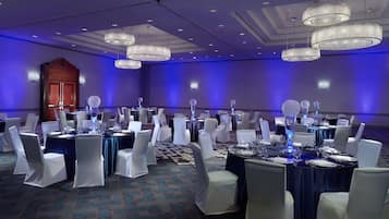 A banquet hall with round tables, white chairs, and blue tablecloths.
